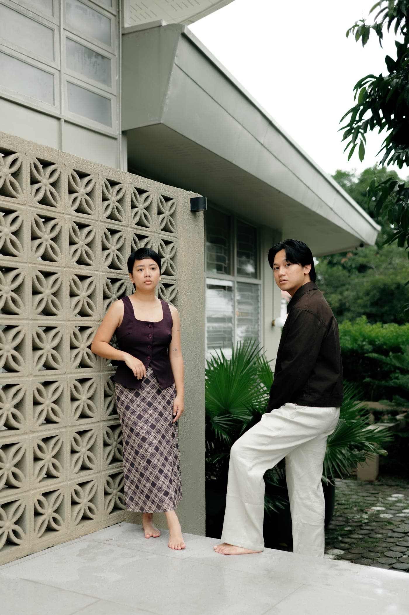 Stefie and Kenn outside the house — she against the breeze-block wall, he on the step beside it.